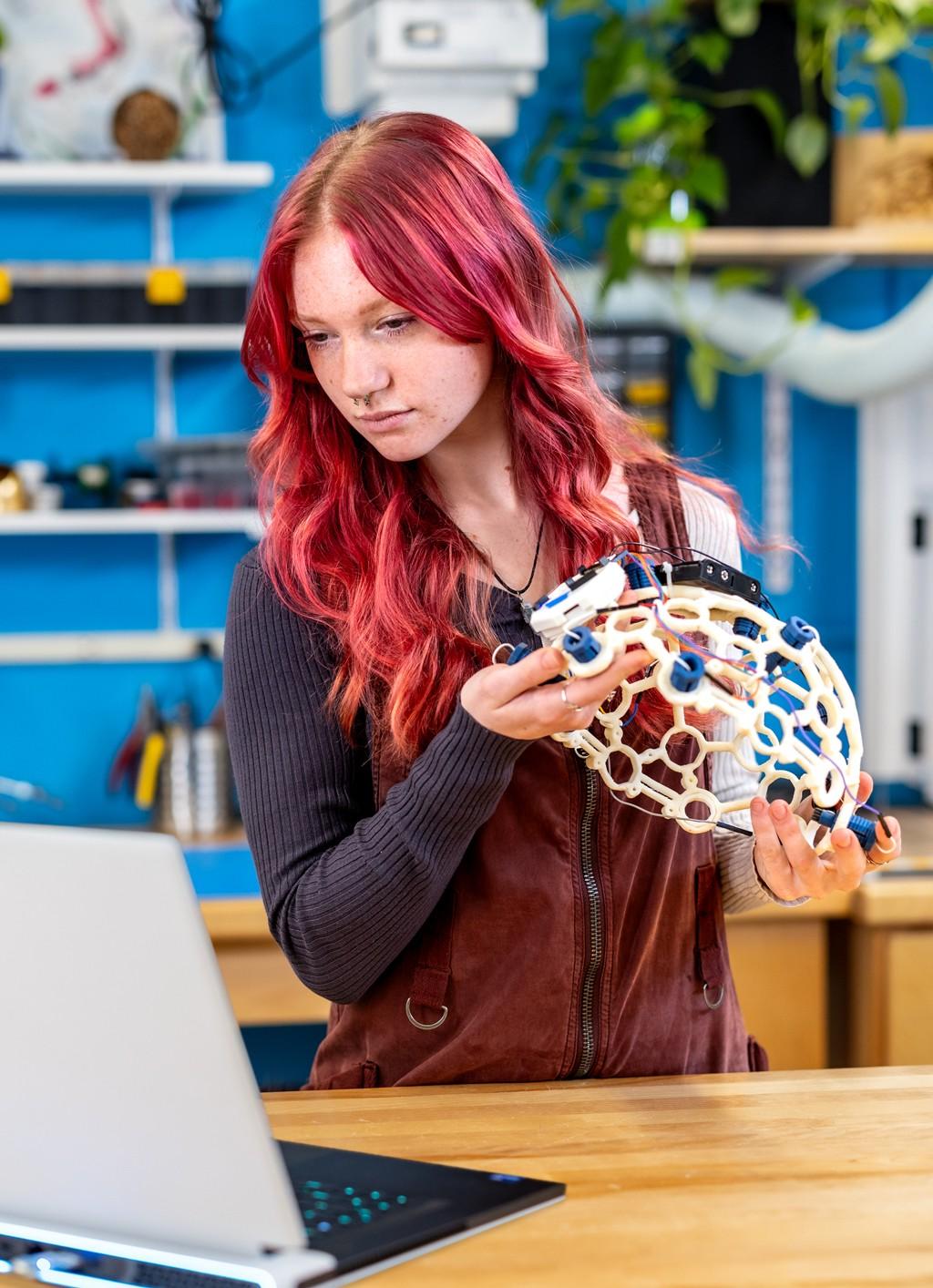 一名计算机科学专业的学生带着脑电波头盔和笔记本电脑站在创客空间里