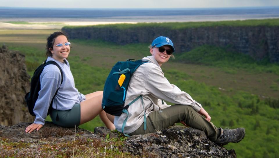 两个英国学生坐在悬崖顶上，俯瞰冰岛的绿色峡谷