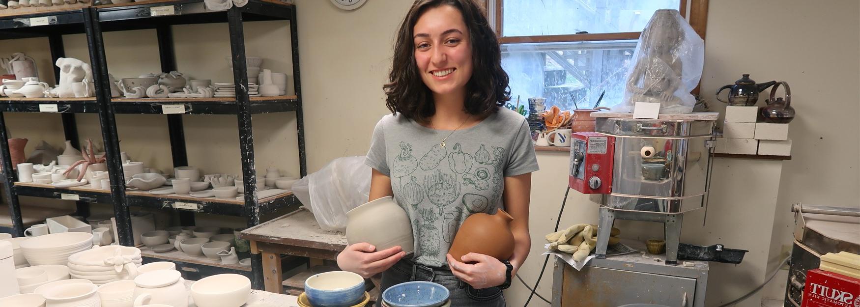 奥利维亚·斯科特站在镜头前微笑着，手里拿着她的手工陶瓷制品