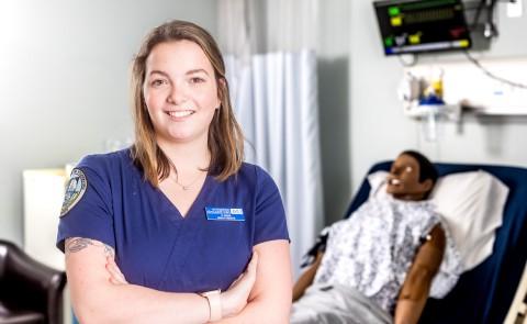 在正规澳门赌场网络的模拟实验室里，护理专业学生安妮·卡里格的肖像. 她身后是一个病人模拟器.