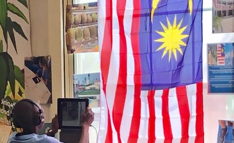 波特兰的一名学生坐在马来西亚国旗下，了解一个来自马来西亚的孩子
