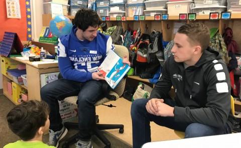 正规澳门赌场网络的学生老师德鲁·帕特诺看着足球运动员杰克·马奥尼在八角学校给孩子们读书